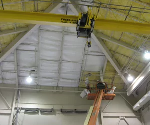 Worker on a crane installing ceiling insulation in a large commercial space.
