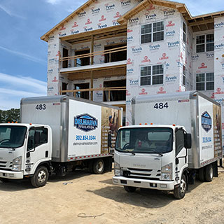 Two Delmarva company trucks parked outside new multifamily construction.