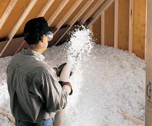 Worker installing blown-in insulation in an attic floor.