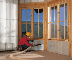 Worker installing blown-in insulation beneath an interior window.