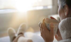 Woman wearing slippers and sipping from a warm mug on a sunny winter morning.