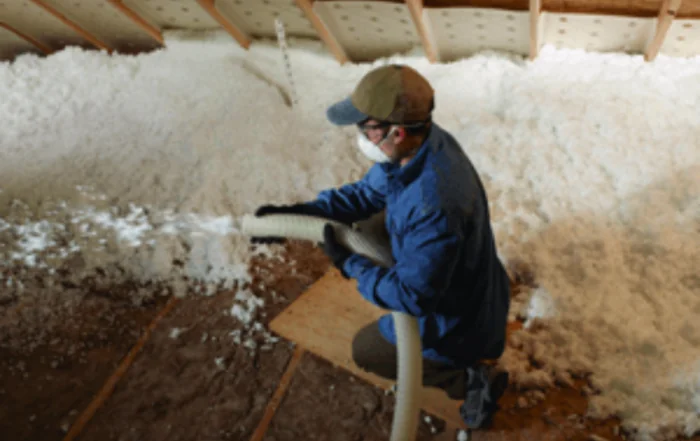 Worker blowing cellulose insulation in attic