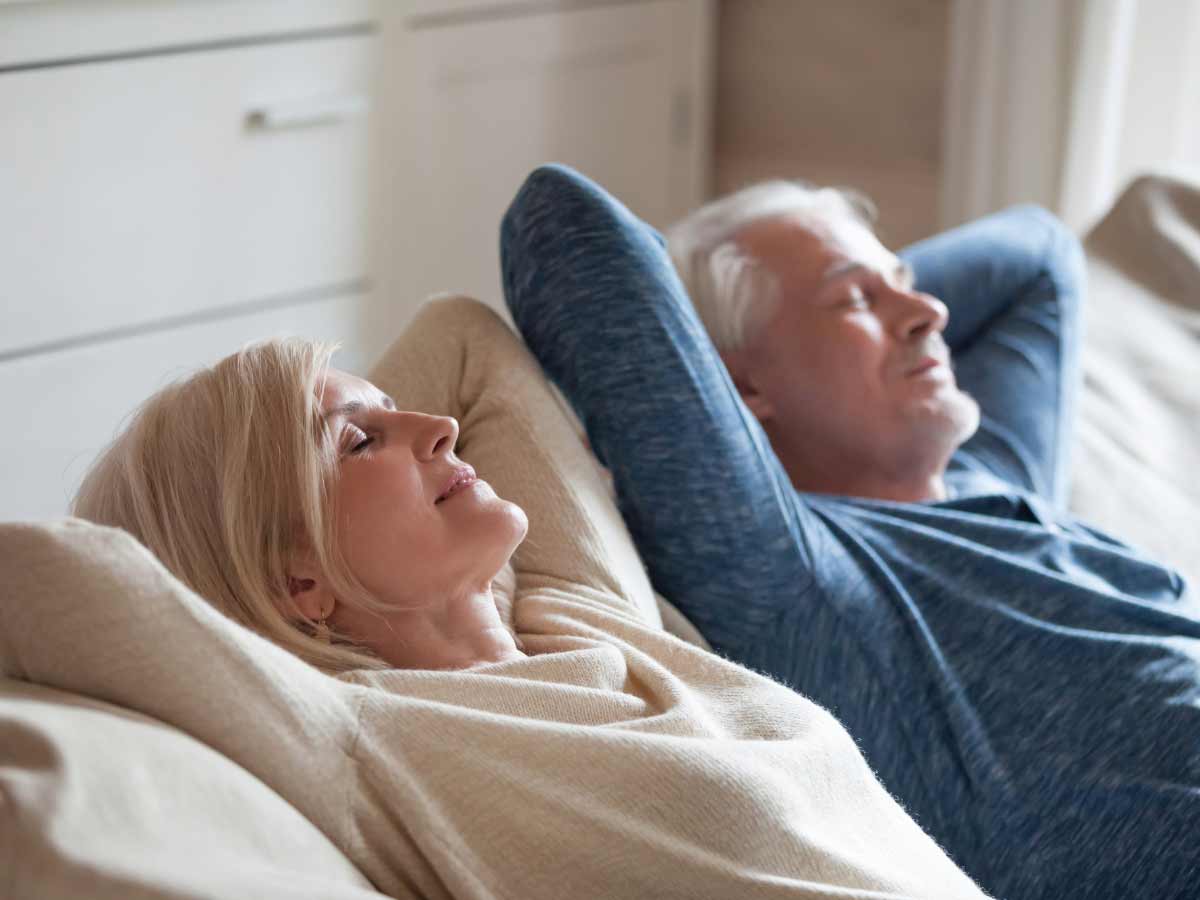 Elderly couple breathing in fresh air, while reclining back on living room couch.