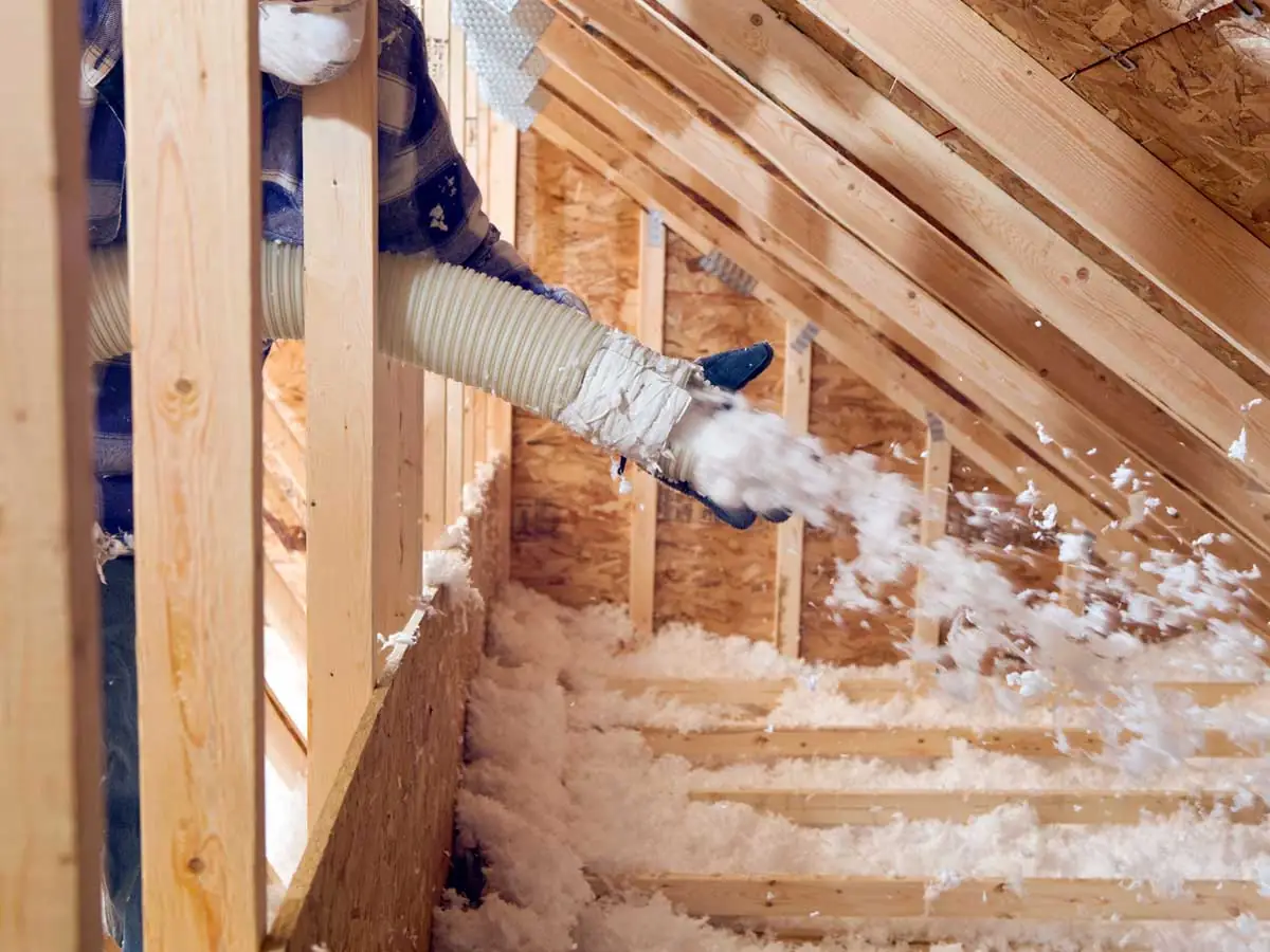 Worker blowing loose-fill insulation into attic space.