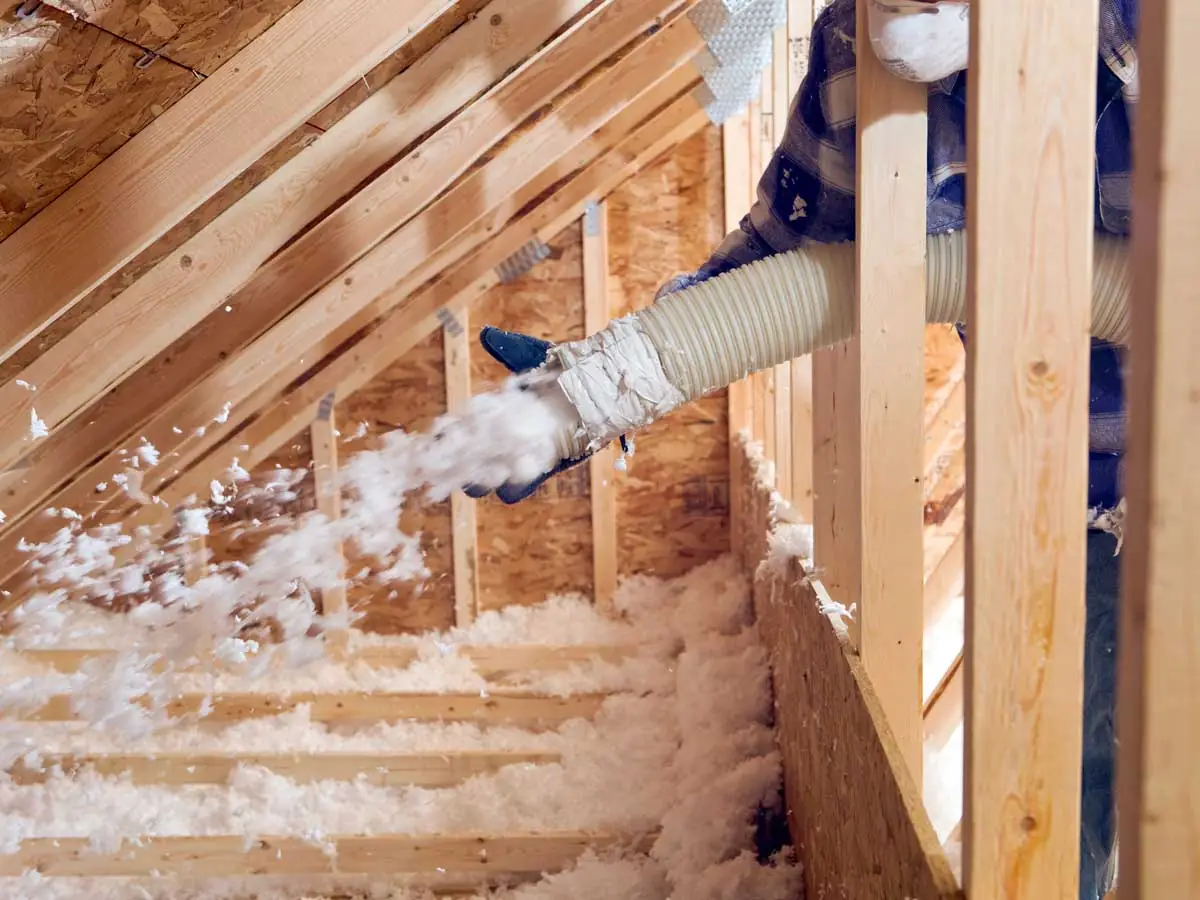 Another view of worker blowing attic insulation.