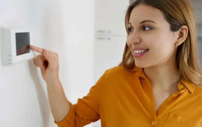 Woman in orange shirt smiling and turining on smart thermostat
