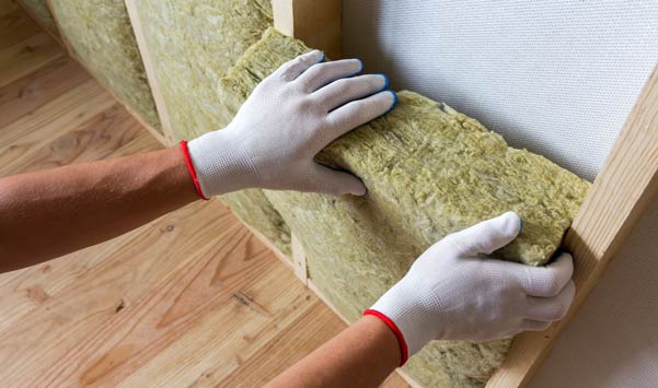 Gloved hands installing fiberglass insulation batt.