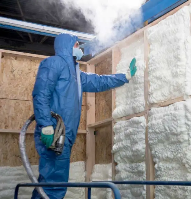 Worker spraying foam insulation onto wall panel