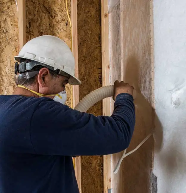 Worker insulating walls with a blown-in wall insulation system.