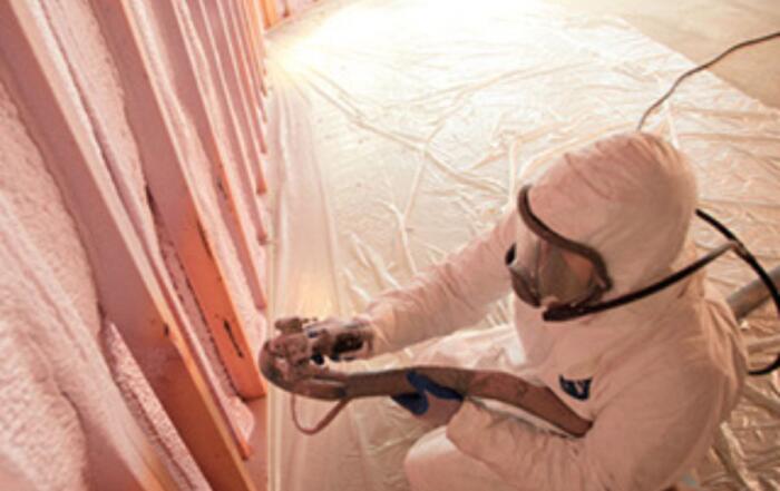 Worker spraying foam insulation in attic rafters