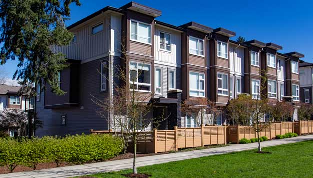 A row of modern townhomes with large windows, wooden fencing, and landscaped sidewalks, representing a completed multifamily dwelling.