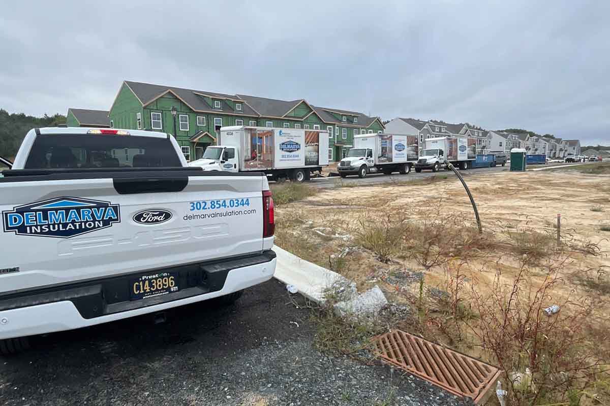 Branded Delmarva Insulation trucks and vans parked at a residential construction site with new homes in the background.