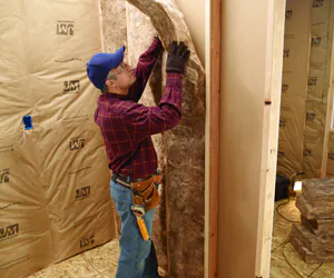 Person in plaid shirt installing fiberglass insulation in a framed wall