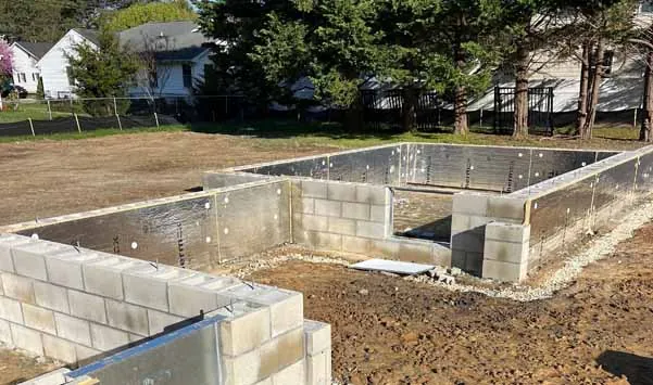 Image showing the early stage of a residential construction site with newly installed concrete block foundation walls. Insulation board is applied for thermal efficiency and waterproofing.