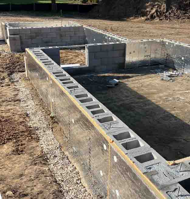 A closer view of concrete block walls lined with insulation board at a home construction site, demonstrating the alignment and sealing of the wall structure.