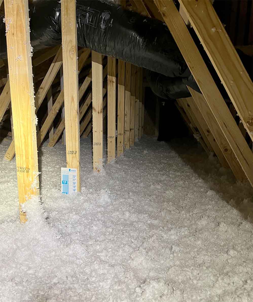 Blown-in loose-fill fiberglass insulation covering attic floor with R-value depth gauge, installed by Delmarva Insulation.