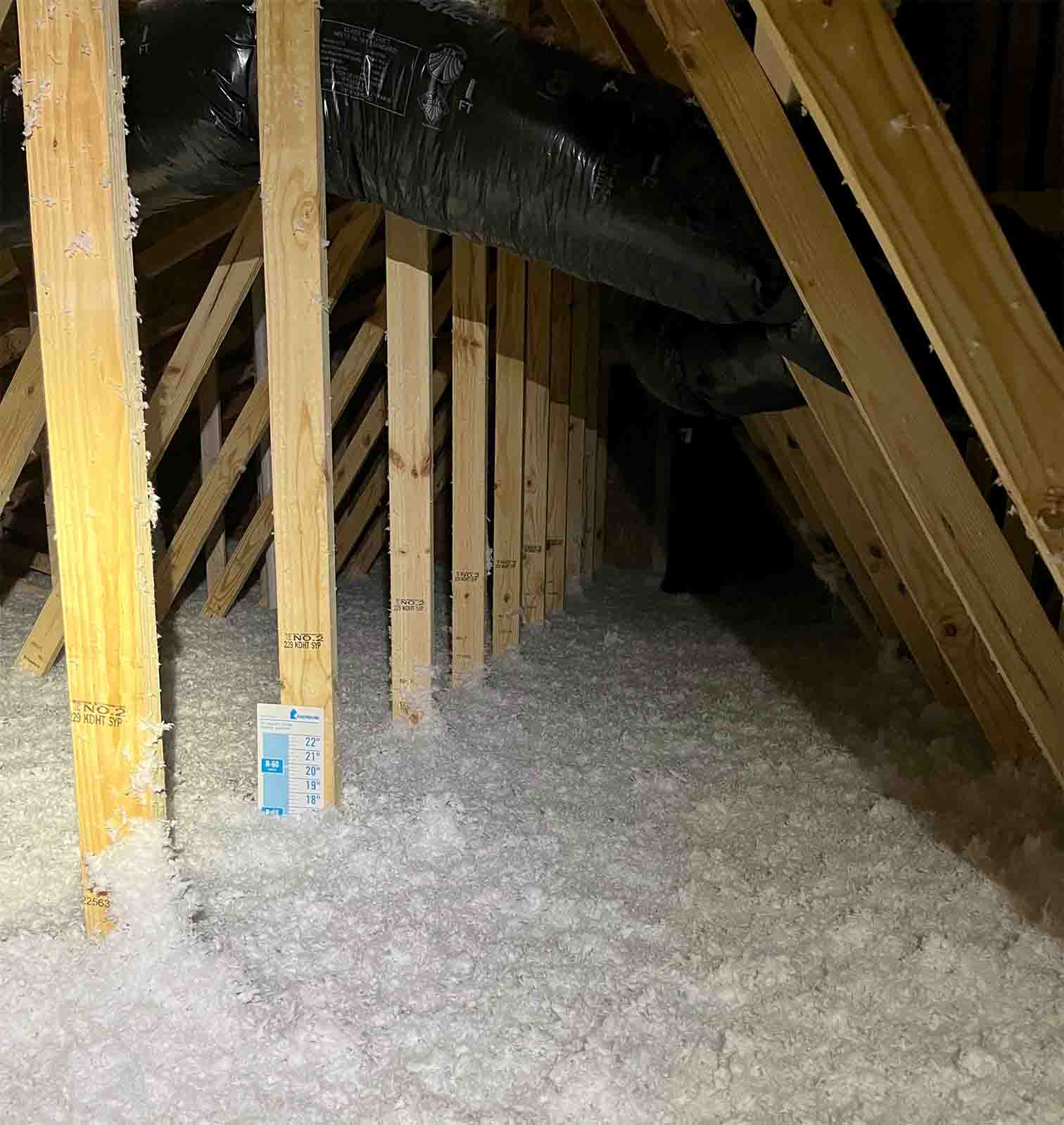 Delmarva Insulation blown-in fiberglass insulation covering an attic floor between roof trusses, with an insulation.